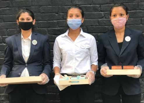 Three waitress wearing facemasks with trays in their hands