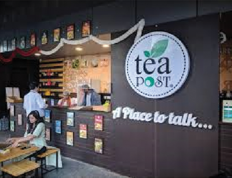 A group of people standing on either side of the counter with Tea Post logo on the wall
