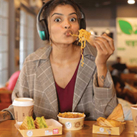 A woman wearing a pair of headphones slurping the noodles